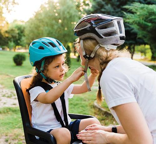 photo of a child in seat on back of a bicycle who is helping their mom fastern her 头盔